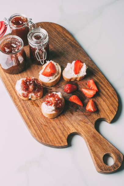 top view of cutting board with fruit jam in jars and sandwiches with cream cheese and jam on marble table - 写真・画像