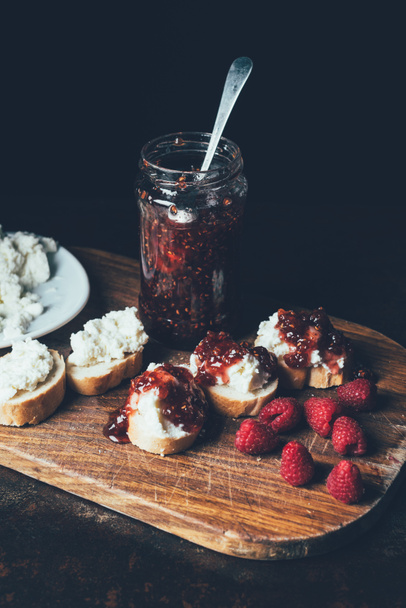 elevated view of raspberries, sandwiches with fruit jam and cream cheese on cutting board on black  - Zdjęcie, obraz