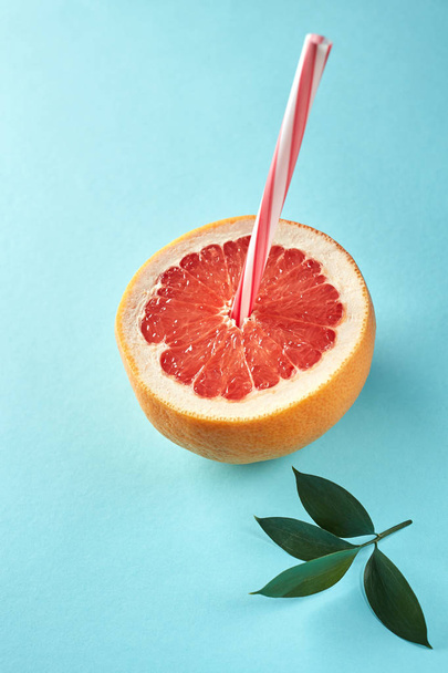 Fresh sliced grapefruit wih straw and green leaves on blue background. Idea creative to produce work within an advertising marketing communications. Business concept - Фото, зображення