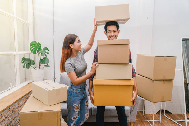 Asian young couple carrying big cardboard box for moving in new house, Helping relocate and joshing together, Moving and House Hunting concept, selective focus - Photo, Image