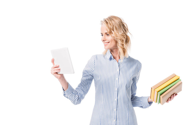 smiling attractive woman looking at tablet and holding books isolated on white - Foto, immagini
