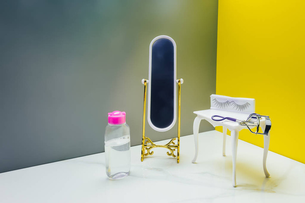 toy mirror and dressing table with bottle of lotion and eyelash curler in miniature room - Photo, Image