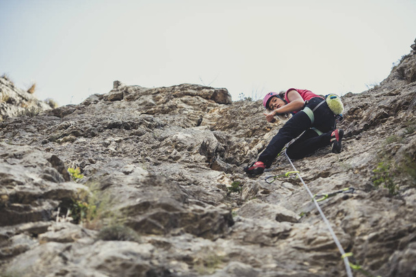 From below photo of a woman climber climbing a rock. - Foto, Bild