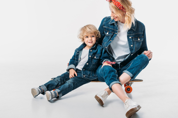 smiling mother and son sitting on skateboard on white - Foto, Imagen
