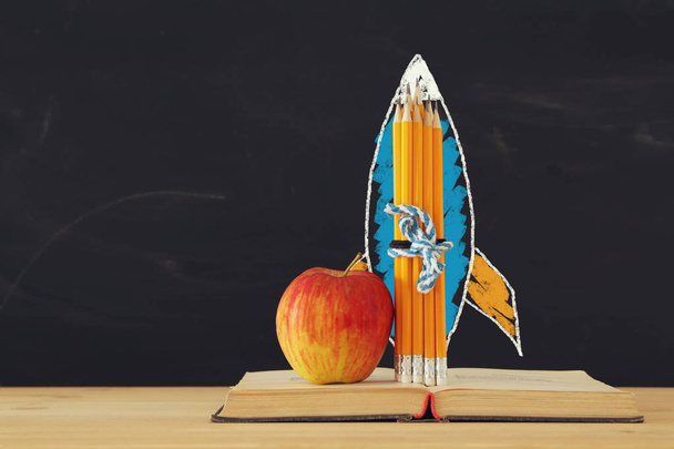 Back to school concept. rocket sketch and pencils over open book in front of classroom blackboard - Photo, image