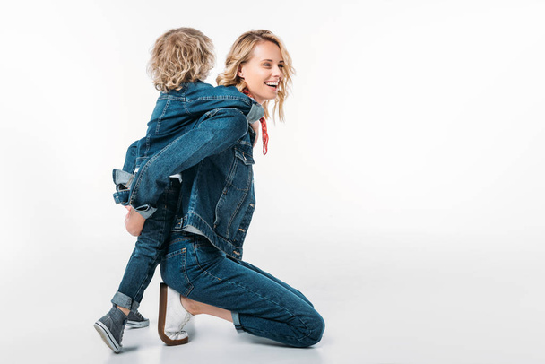 side view of happy mother giving piggyback to son on white - Fotoğraf, Görsel