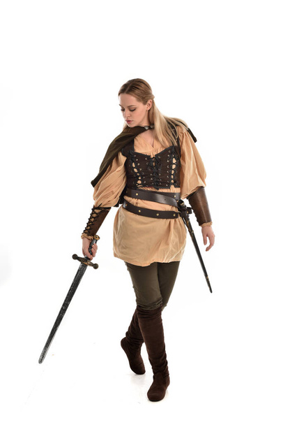 Portret van de volledige lengte van blond meisje bruin middeleeuwse strijder kostuum dragen. staande pose, geïsoleerd op witte studio achtergrond. - Foto, afbeelding