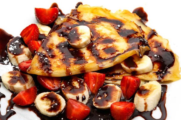 Pancakes with strawberries, bananas and chocolate syrup on white background - Fotó, kép