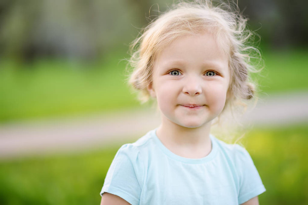 Cute toddler girl outdoors portrait in summer day. Smiling and charming child. Little lady with blonde and curly hair - 写真・画像
