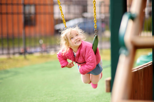 Cute little girl having fun on outdoor playground. Spring/summer/autumn active sport leisure for kids. Child on plastic swing - Photo, Image