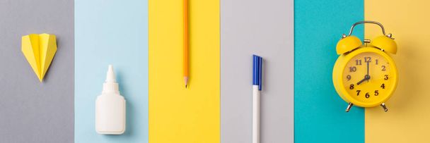 school and office supplies on bright striped background. minimum set: pen, pencil, glue, alarm. concept: back to school, minimalism. Flat lay, top view long banner - Zdjęcie, obraz