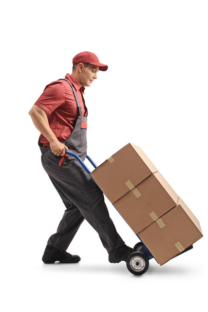 Full length profile shot of a mover with a hand truck loaded with cardboard boxes isolated on white background - Fotó, kép