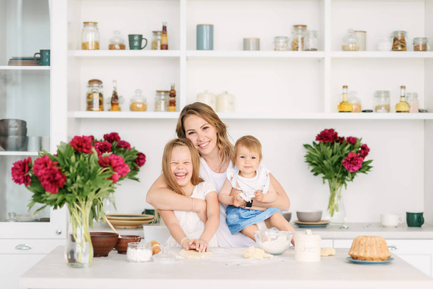 A young mother with her two children is preparing tasty and healthy food in a large and bright kitchen. woman teaches children how to make dough - Φωτογραφία, εικόνα