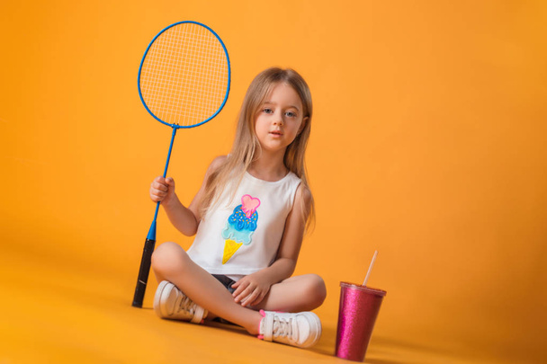 Little girl posing with a tennis racket and a shaker in the studio - 写真・画像