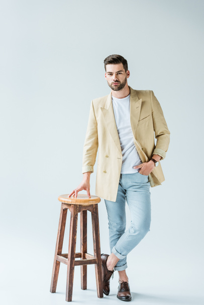 Fashionable confident man leaning on stool on white background - Фото, изображение