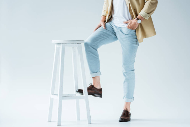 Cropped view of stylish young man leaning on stool on white background - Zdjęcie, obraz