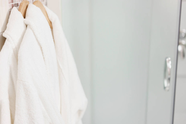 Schone witte handdoek en badjas op een hanger bereid te gebruiken. Badkamer binnen kamers van een appartement of hotel. - Foto, afbeelding