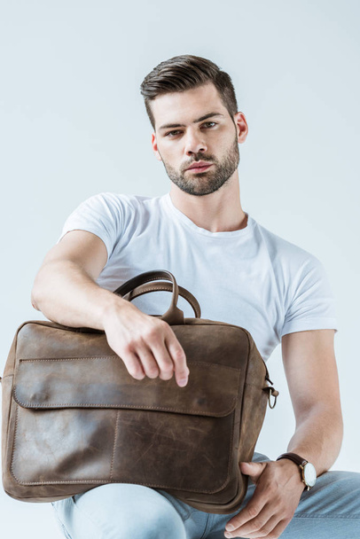 Stylish young man sitting and holding briefcase isolated on white background - Photo, Image