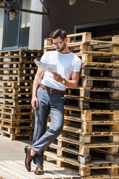 Empresario confiado de moda fumando cigarro y leyendo informe por paletas de madera
 - Foto, Imagen