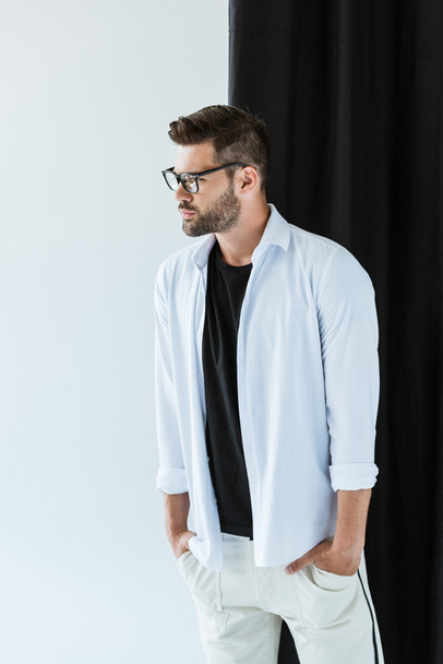 Homem elegante e confiante vestindo óculos e camisa branca em pé por cortina preta
 - Foto, Imagem