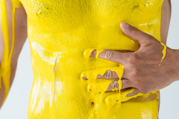 Vista cortada do corpo masculino coberto com tinta amarela isolada sobre fundo branco
 - Foto, Imagem