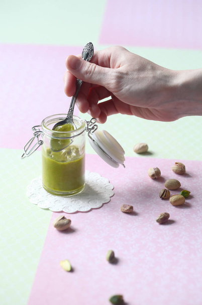 Pasta de pistache caseiro em um pote de vidro pequeno, em fundo verde claro e rosa
. - Foto, Imagem