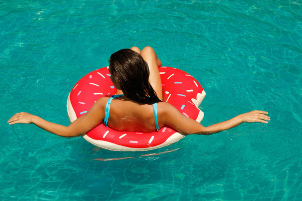 Beautiful young woman and inflatable swim ring in shape of a donut in pool - Foto, Imagem