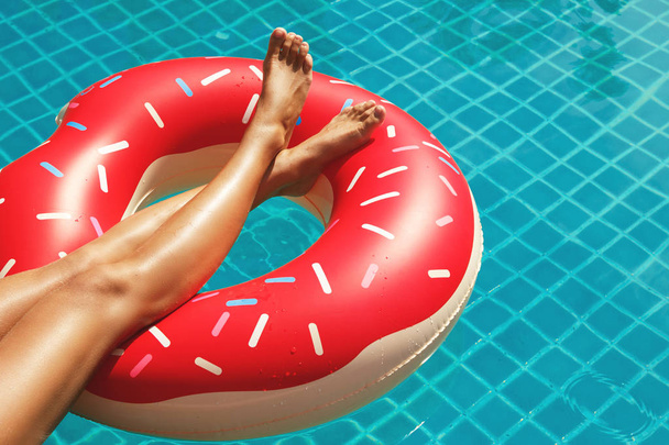Female legs and inflatable swim ring in shape of donut in the pool - Foto, afbeelding