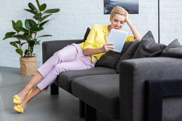 smiling young stylish woman using digital tablet on sofa at home - Фото, зображення