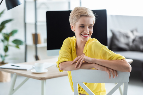 вибірковий фокус усміхненої бізнес-леді, що сидить біля столу з комп'ютером в офісі
  - Фото, зображення