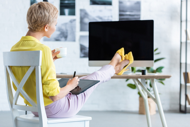 女性フリーランス コーヒーを飲むと、グラフィック タブレットを使用してホーム オフィスのコンピューターを持つテーブルでの選択と集中  - 写真・画像