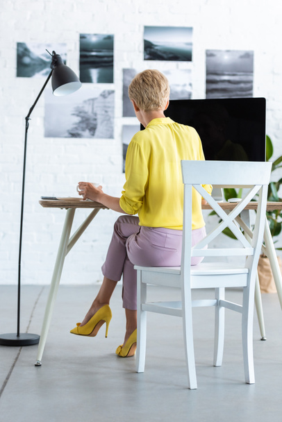 задний вид деловой женщины, пьющей кофе и работающей за компьютером за столом
  - Фото, изображение