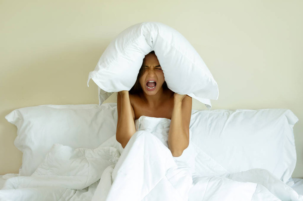 Woman with pillow on her head because she dont wanna hear noise - 写真・画像