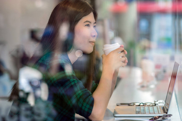 Портрет азійської бізнесменки в повсякденному пияцтві костюмів і роботі з технологічним ноутбуком в акції щастя за столом поруч зі склом в сучасному офісі, власник бізнесу і концепція підприємця - Фото, зображення