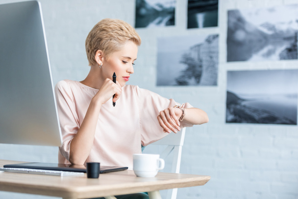 freelance donna che guarda orologio da polso a tavola con tablet grafico e computer in home office
  - Foto, immagini