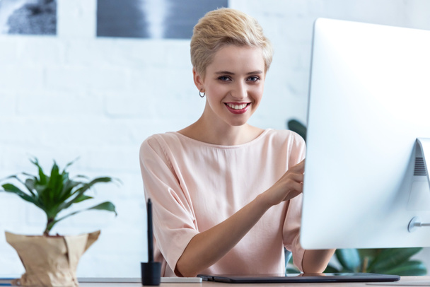 улыбающаяся деловая женщина, работающая за столом с компьютером в офисе
 - Фото, изображение