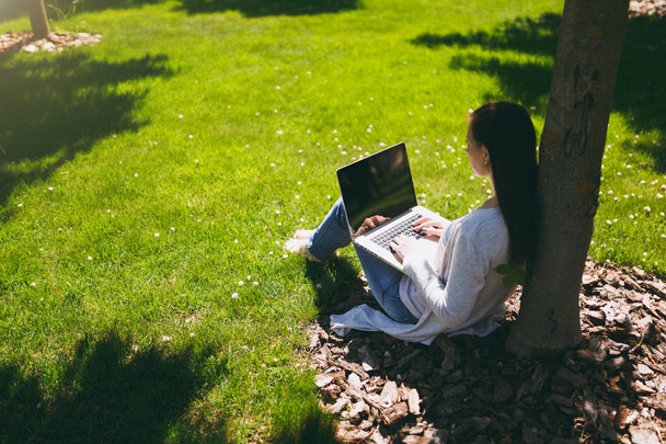 Young successful businesswoman in casual clothes. Woman sit on grass ground, working on laptop pc computer in city park on green lawn outdoors on nature. Mobile Office. Freelance business concept - Foto, afbeelding
