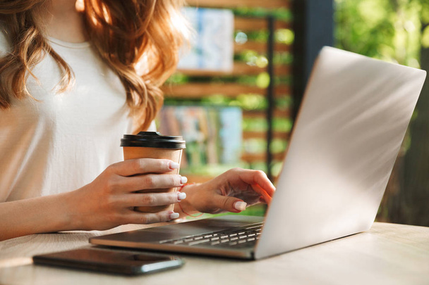 Gros plan d'une femme tapant sur un ordinateur portable à la table et tenant une tasse de café à l'extérieur
 - Photo, image