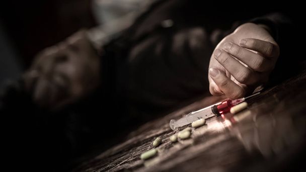 Hombre drogadicto acostado en la llaga cerca de la jeringa para inyección de drogas y pastillas. Muerte por sobredosis de drogas y concepto de adicción
 - Foto, Imagen