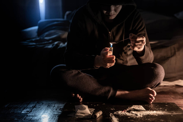 Homem drogado preparando dose de heroína usando colher e isqueiro para derreter, Seringa para injeção. Conceito de overdose e dependência de drogas duras
 - Foto, Imagem