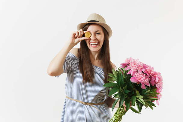 Jonge vrouw in jurk, muts houdt bitcoin, munt van gouden kleur, mooie roze pioenrozen bloemen boeket geïsoleerd op een witte achtergrond. Zakelijke, levering, online winkelen, virtuele valuta concept - Foto, afbeelding
