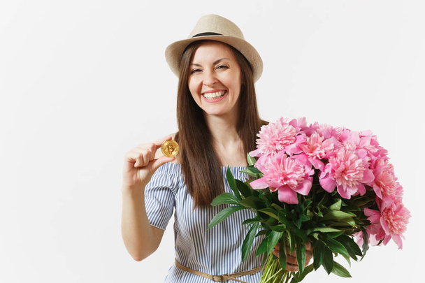 Young woman in dress, hat holding bitcoin, coin of golden color, bouquet of beautiful pink peonies flowers isolated on white background. Business, delivery, online shopping, virtual currency concept - Foto, afbeelding