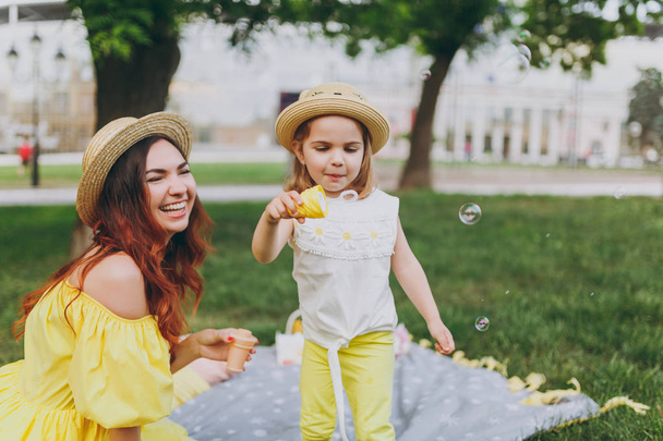 黄色い服の女性は笑って公園残りでプレーし、石鹸泡送風機を保持小さなかわいい子赤ちゃん女の子と楽しい時を過します。母親、子供の幼い娘。母の日、愛の家族、親、子供の頃 - 写真・画像