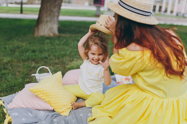 Frau in gelben Kleidern spielen auf grünem Rasen im Park, ruhen und haben Spaß mit kleinen niedlichen Baby-Mädchen. Mutter, kleine Tochter. Muttertag, Liebe Familie, Elternschaft, Kindheitskonzept - Foto, Bild