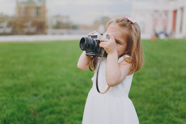 Malé krásné dítě holčičku v lehkých šatech se vyfotit na retro vinobraní fotoaparát na zelené trávě v parku. Matka, dítě dceruška. Den matek, láska rodina, rodičovství, dětství koncept - Fotografie, Obrázek