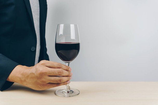 man in grey shirt and black suit putting a glass of red wine on the wooden table - Foto, afbeelding