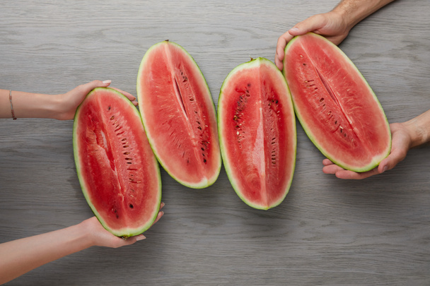 cropped shot of man and woman holding watermelon slices on grey wooden surface - Photo, Image