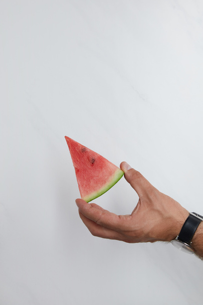 tiro cortado de homem segurando pedaço de melancia em mãos na superfície branca
 - Foto, Imagem