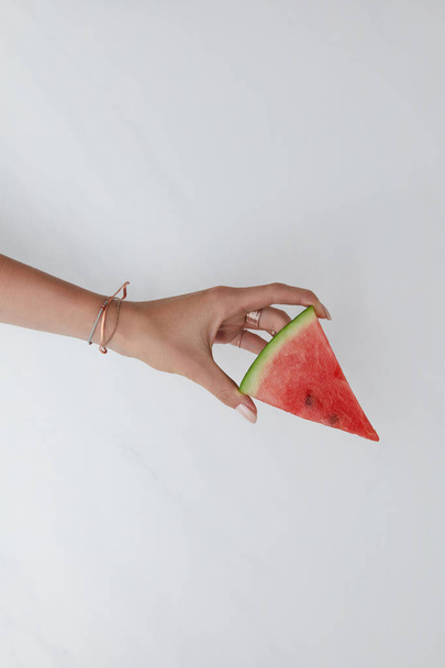 plan recadré d'une femme tenant une tranche de pastèque à la main sur une table blanche
 - Photo, image