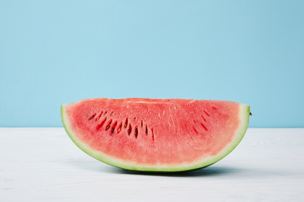 close up view of fresh watermelon slice on white surface on blue background - Fotoğraf, Görsel